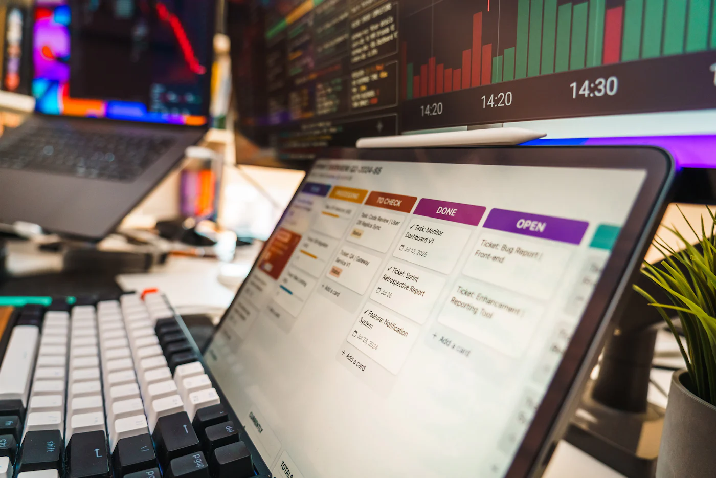Tablero de tareas por etapas en una tablet, junto a monitores con datos.